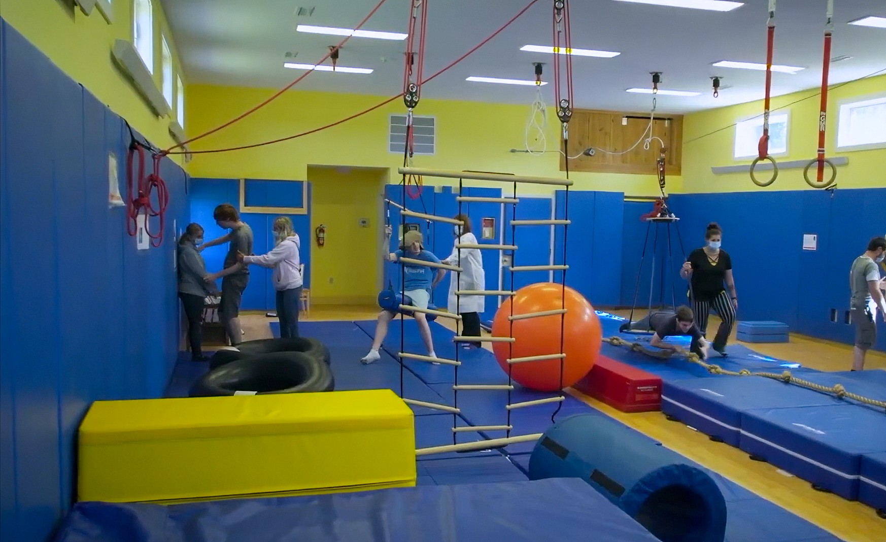 Kids and healthcare workers in a room of mats and apparatuses